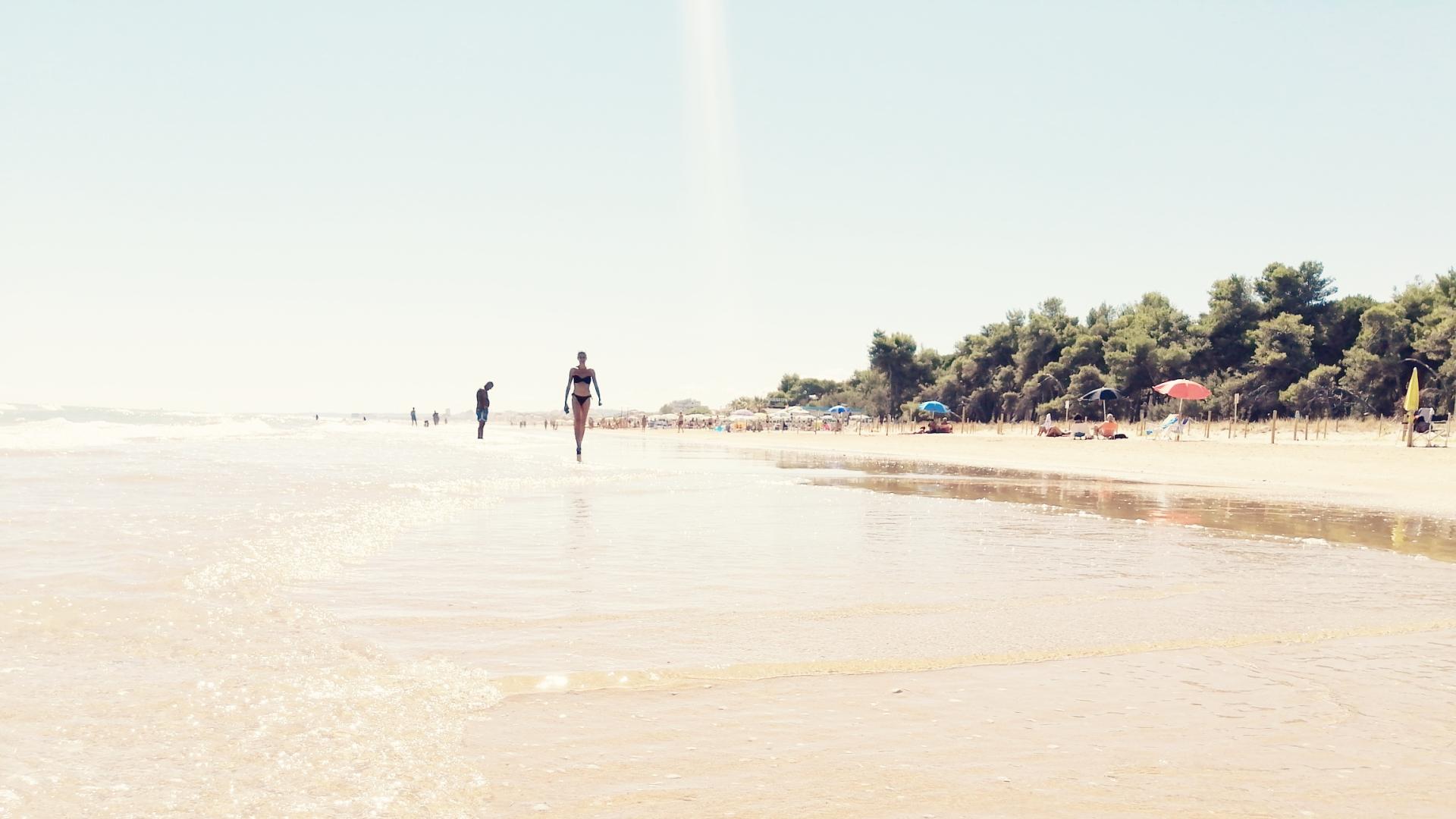 Spiaggia soleggiata con persone che camminano vicino all'acqua.