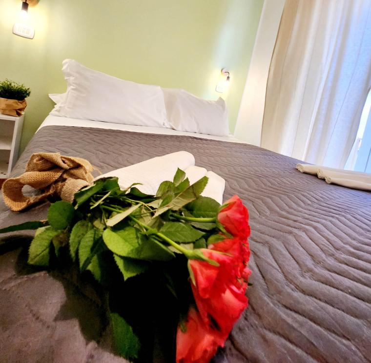 Camera accogliente con letto, cuscini bianchi e rose rosse.